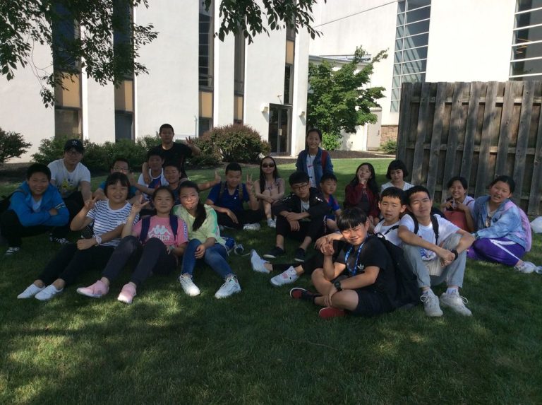 Group of international students sitting on the grass in the shade on a summer day